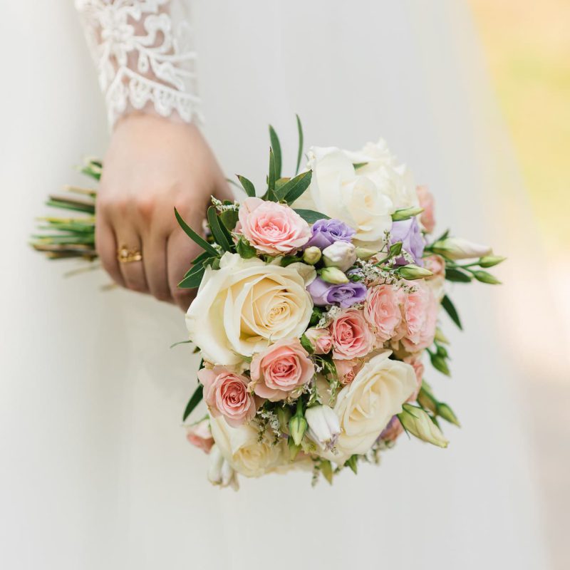The hands of a young bride are holding a beautiful delicate wedding bouquet. Bride's hand with a wedding ring on her finger. Bride in white dress